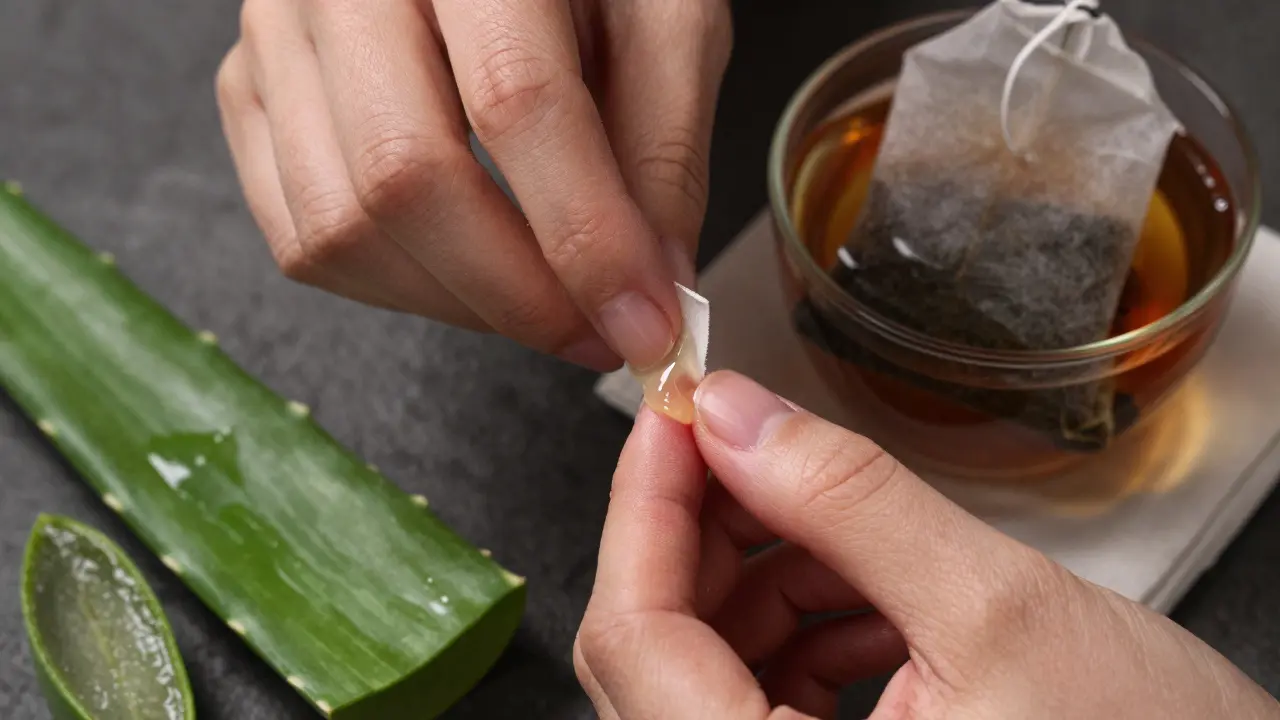 Ruka nanáší čistý gel aloe vera na zánětlivé dásně s čerstvým listem a čajovým pytlíkem.